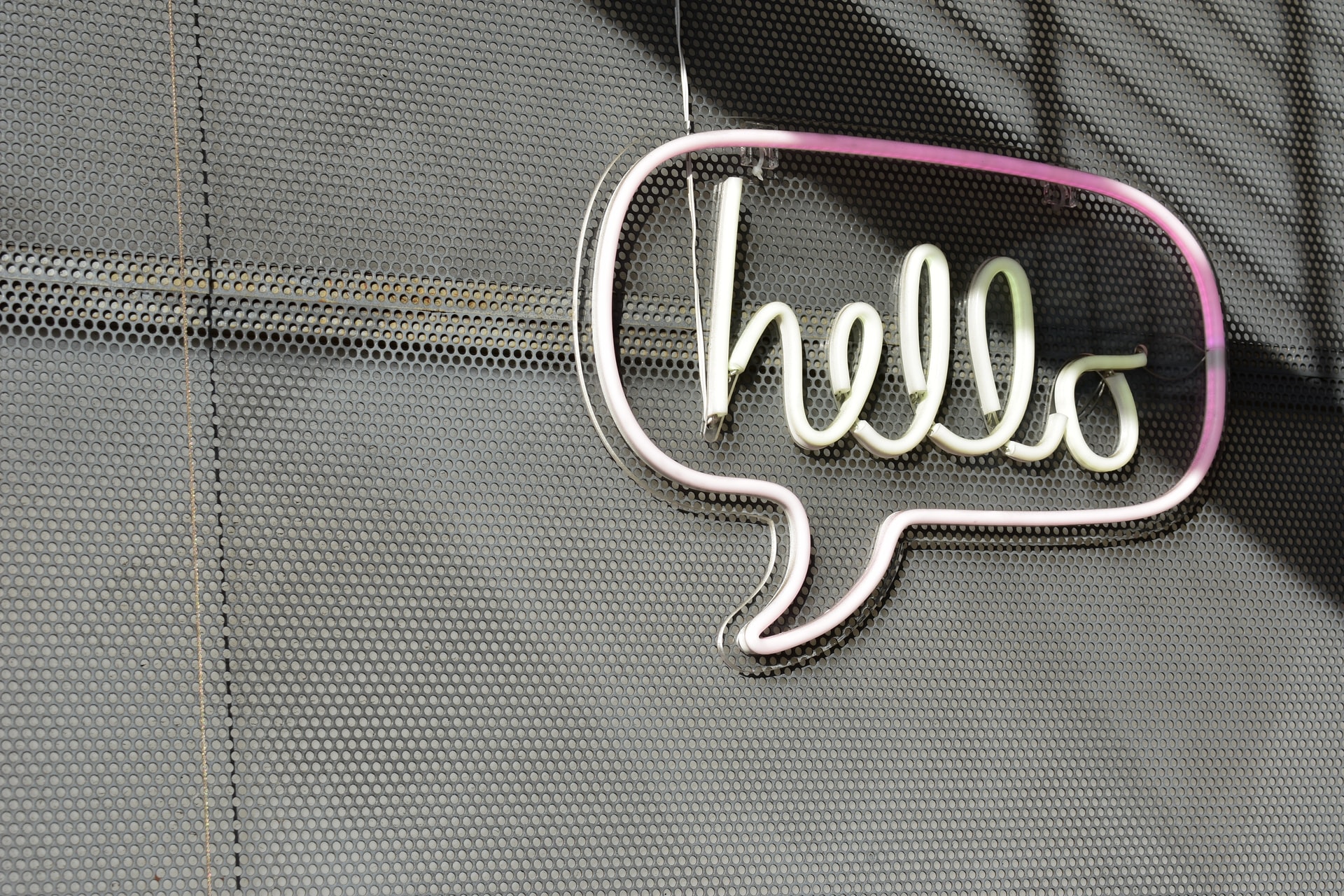 Sprechblase mit Inschrift "hello" aus Neonröhre an Gitterwand