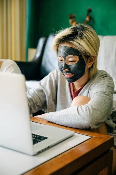 A woman with an applied face mask is sitting from a desk with a laptop.