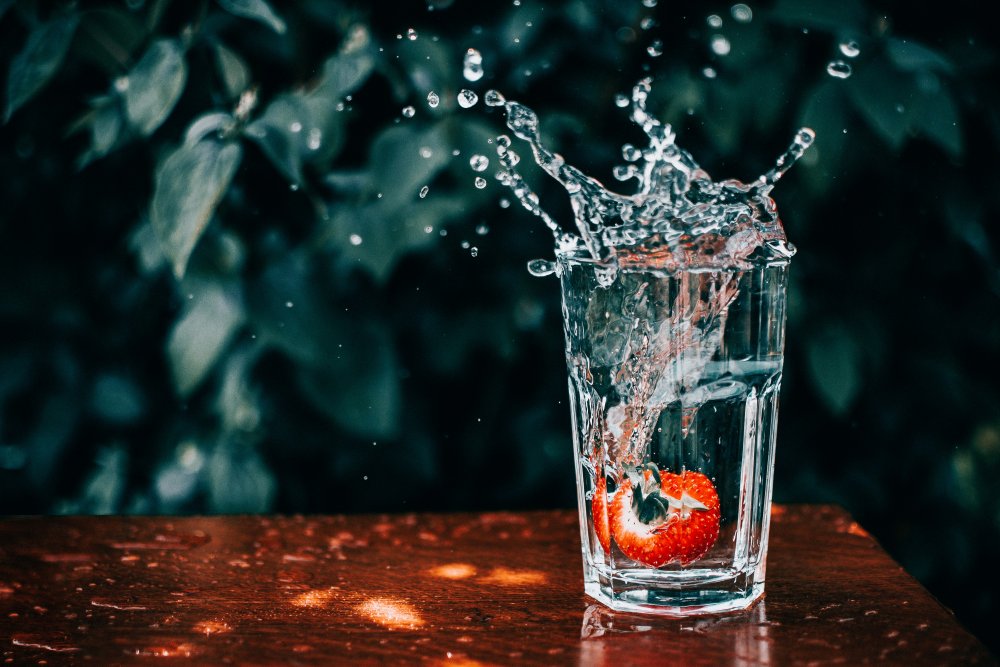 Erdbeere fällt in Wasserglas. Das herausspritzende Wasser ist zu sehen.