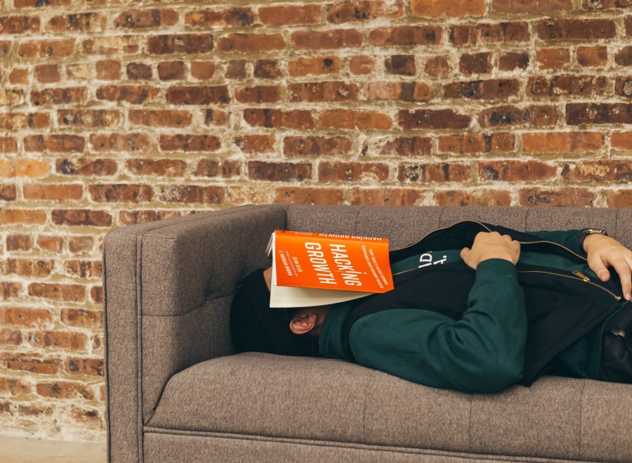 Student schläft mit Buch auf Couch.