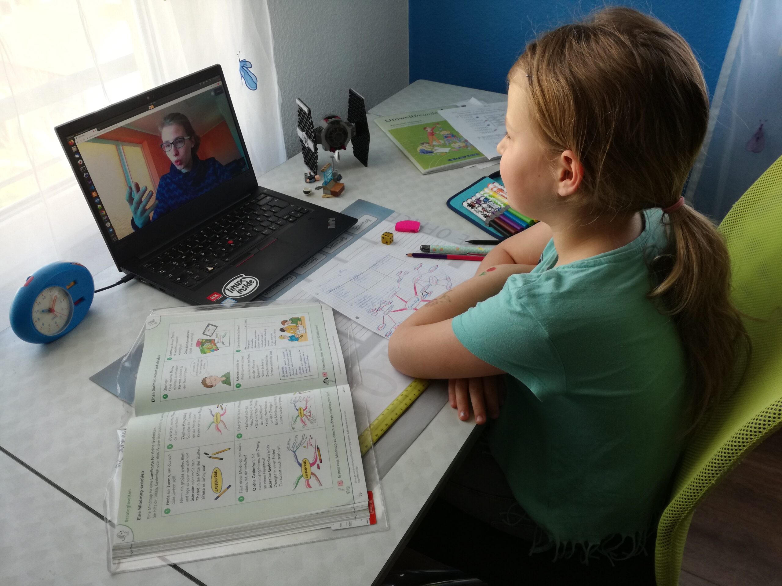 Junges Mädchen vor einem Laptop, auf dem eine Studierende zu sehen ist. Digitale Nachhilfe
