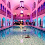 HFDcon 2024: Eine Gruppe von Menschen trifft sich in der rosa-blau angeleuchteten Halle des Stadtbad Oderberger.